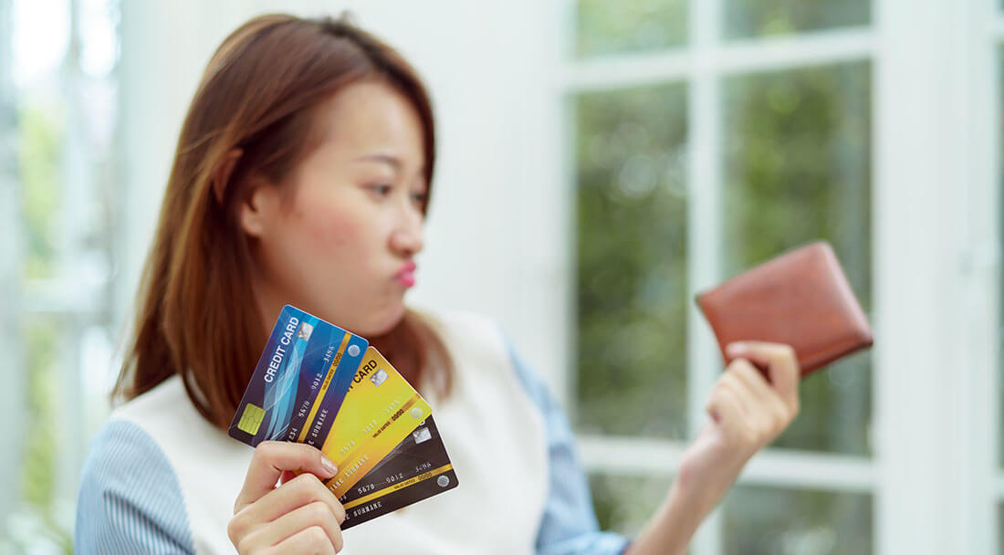 a woman holds her wallet and a stack of credit cards wondering how many credit cards she should have
