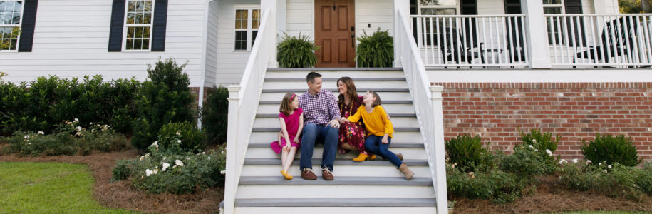 A family of four sitting on the front steps of a house they have a good amount of home equity in.