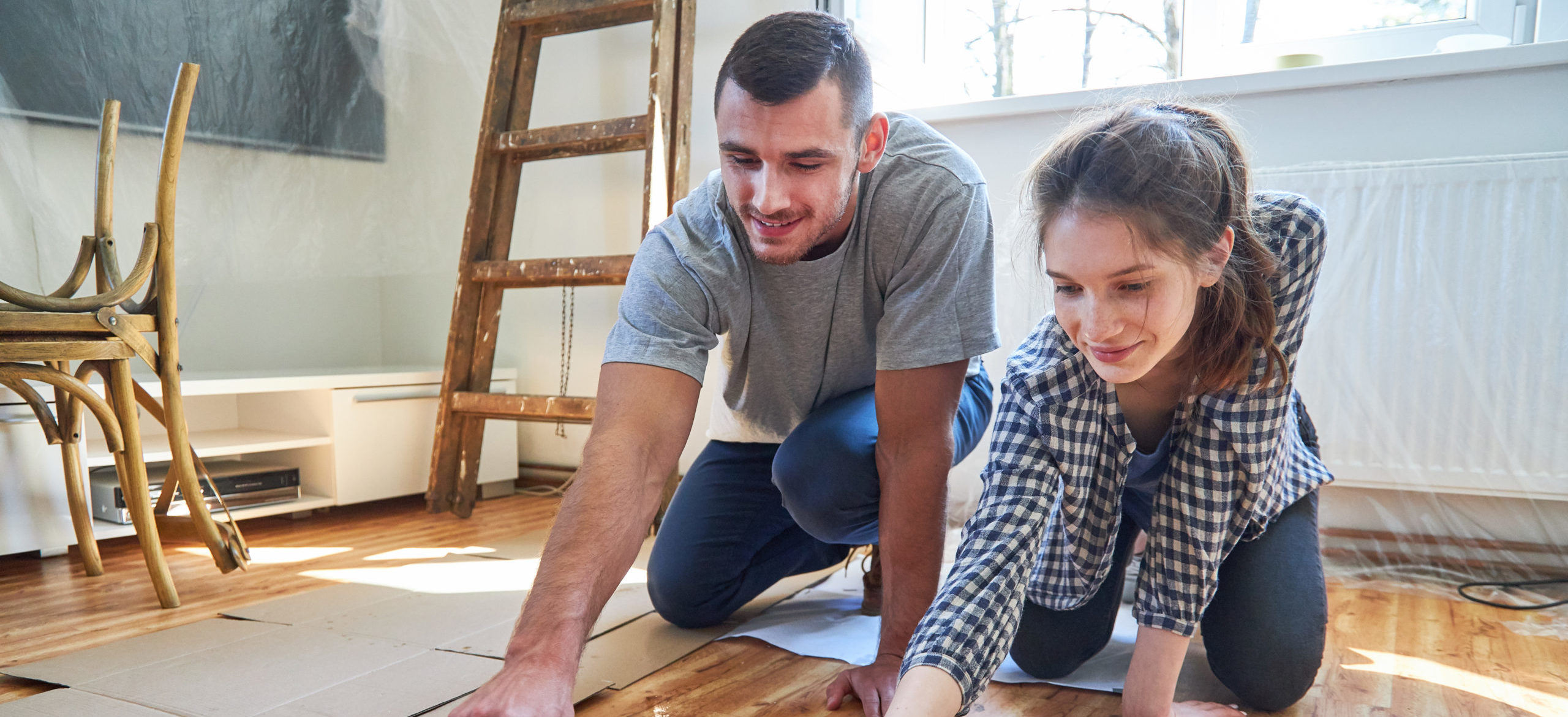 A young couple varnishes their dining room floor as a way to build their home equity with home improvements.