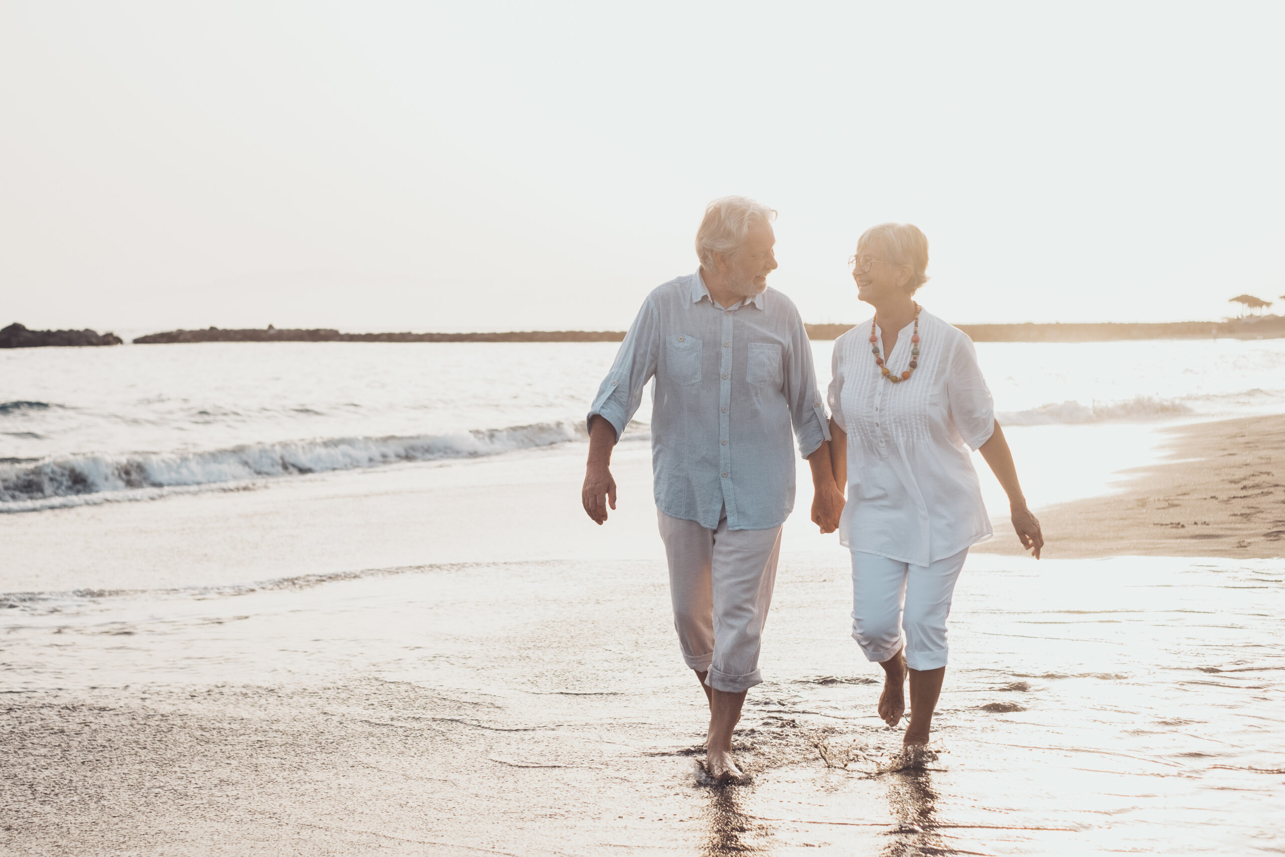 After retiring to a warmer climate using funds from their IRA accounts, a couple takes a leisurely walk on the beach.
