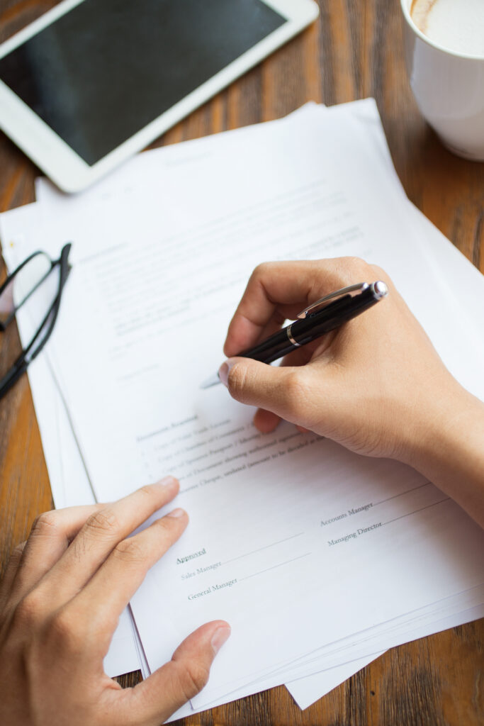 Person filling out a form with a pen on a desk.