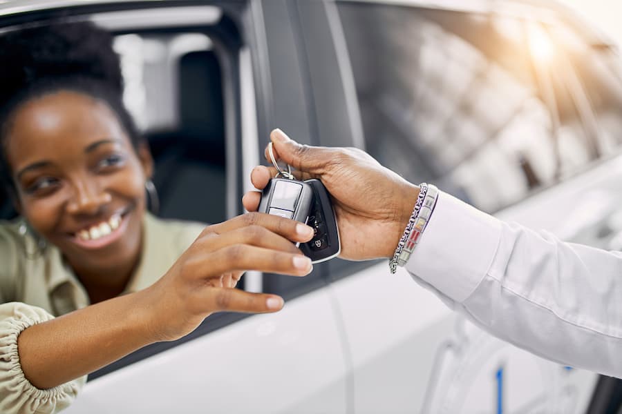 Smiling woman receiving car keys through a vehicle window.