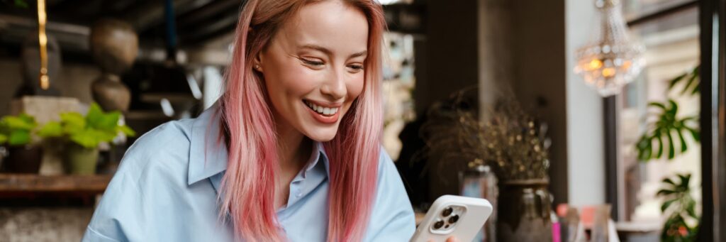 Woman smiling at phone while sitting in a cafe.